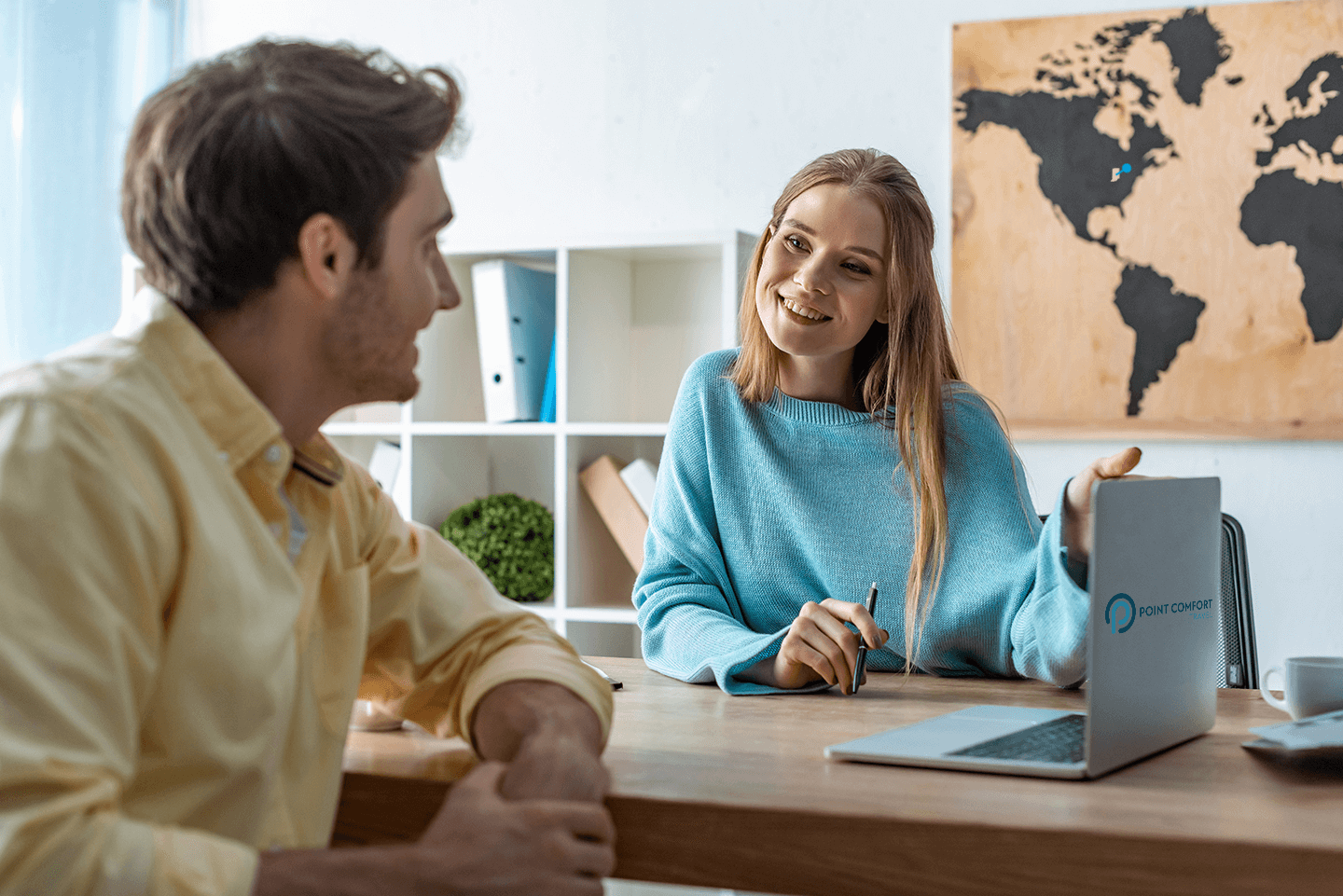 smiling travel insurance agent pointing at laptop screen while talking to client