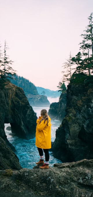 woman in yellow rain jacket standing in front of misty water and hills